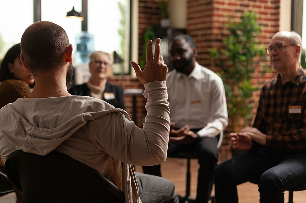 Group of people sitting in a circle with one person raising a hand