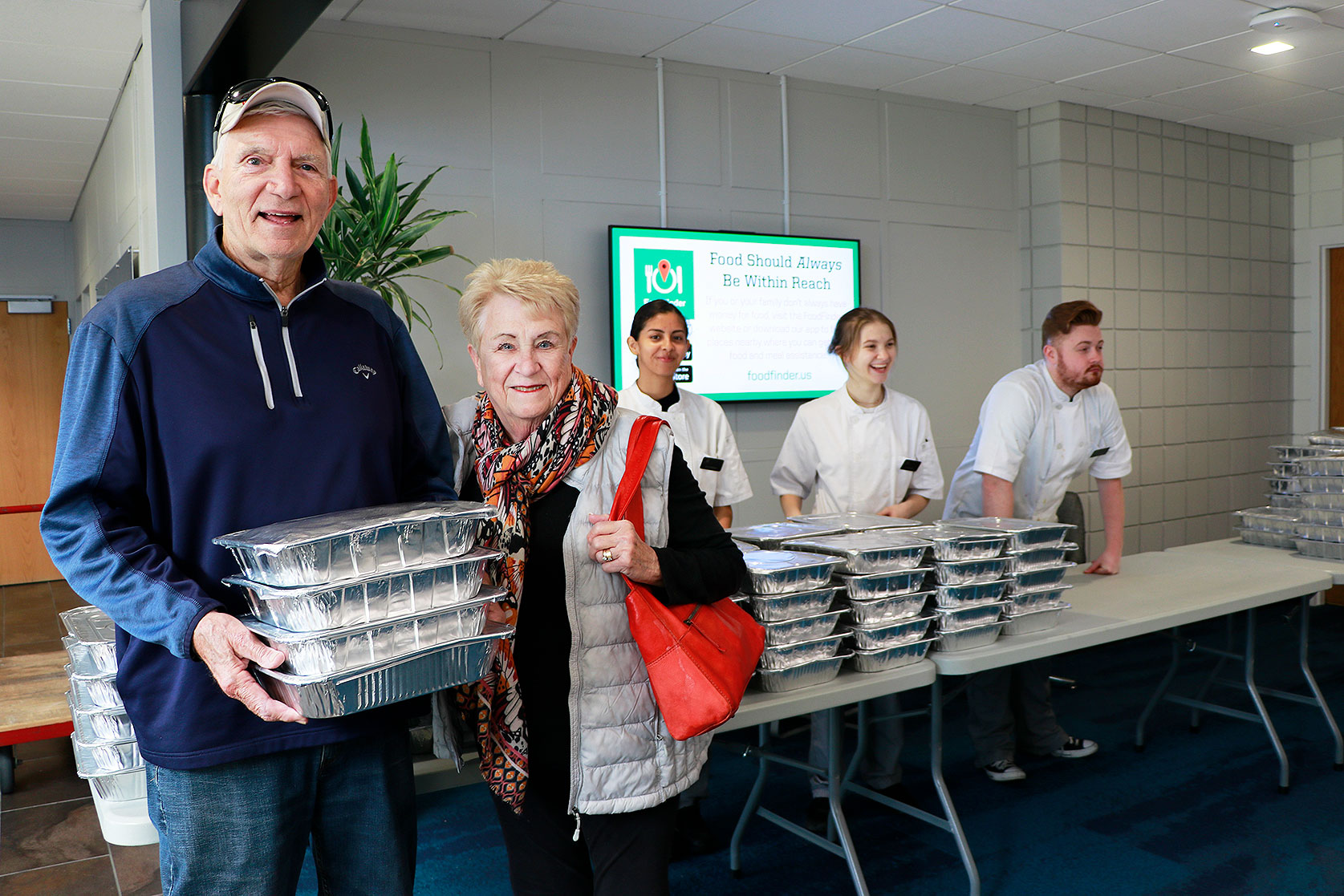 Vern and Nancy Faber (foreground) of Des Moines are all smiles while stopping by the DMACC Urban Campus in downtown Des Moines to pick up their pre-order for four dozen dinner rolls through the DMACC Baking and Pastry Arts program's Fourth Annual Thanksgiving Dinner Roll Fundraiser.