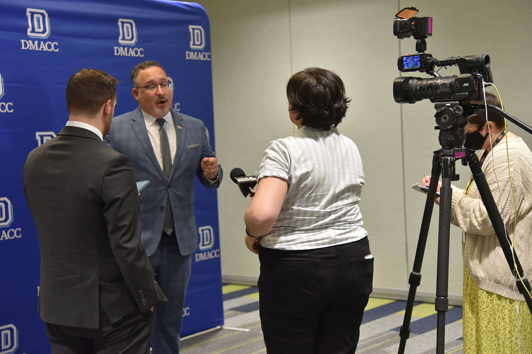 U.S. Secretary of Education Dr. Miguel Cardona (facing camera)​ is interviewed by WOI-TV (ABC 5) photojournalist Rachel Wente (center) and Iowa Capital Dispatch reporter Brooklyn Draisey (right) as ​Sean Sibley (left), Press Secretary at the U.S. Department of Education, listens in on Dec. 7, 2023, at the DMACC Ankeny Campus.