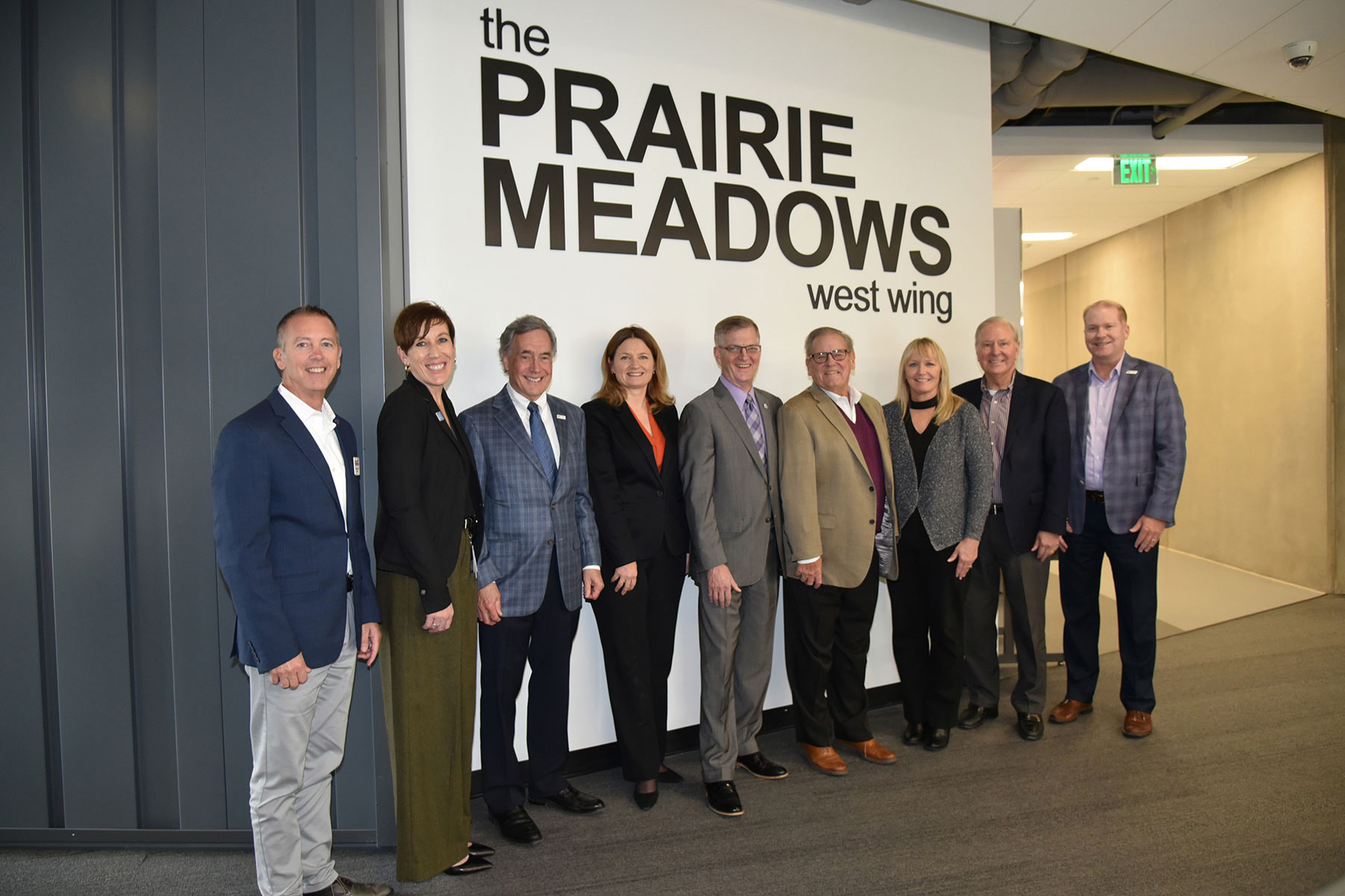 Prairie Meadows, University of Northern Iowa (UNI) and DMACC administrators pose for a photo in front of the Prairie Meadows West Wing signage located on the second floor of the DMACC Urban Des Moines Campus.